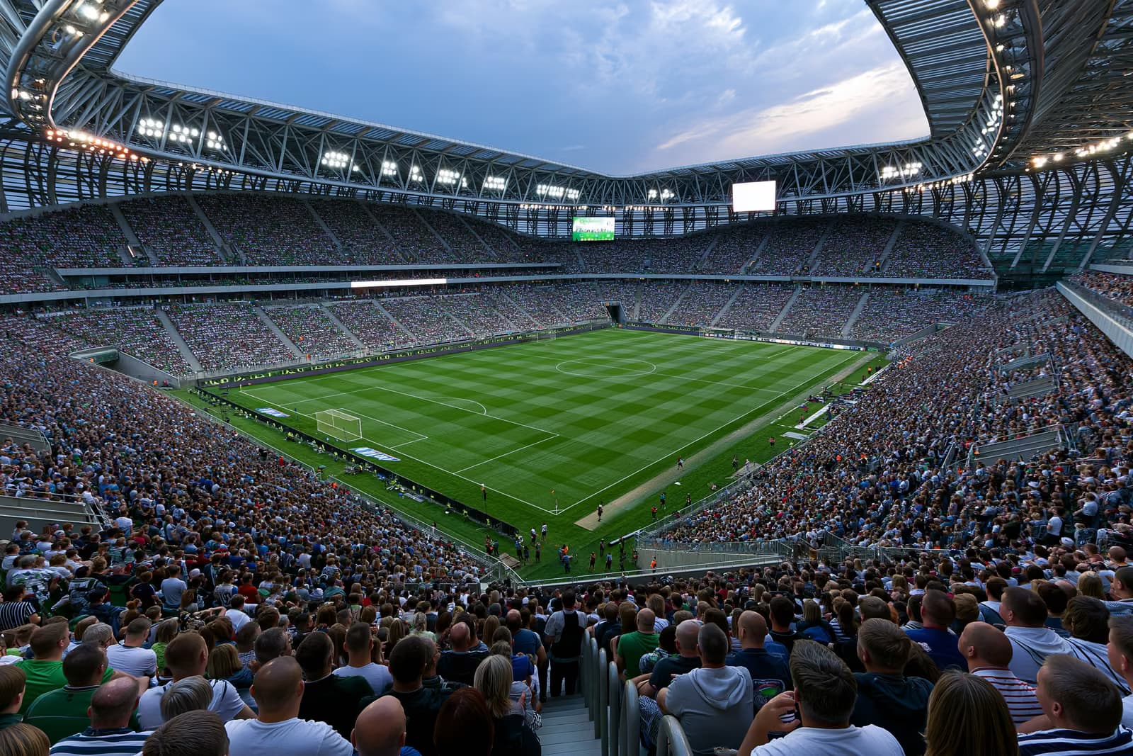 Um grande estádio de futebol lotado de torcedores sob holofotes em uma noite de verão.