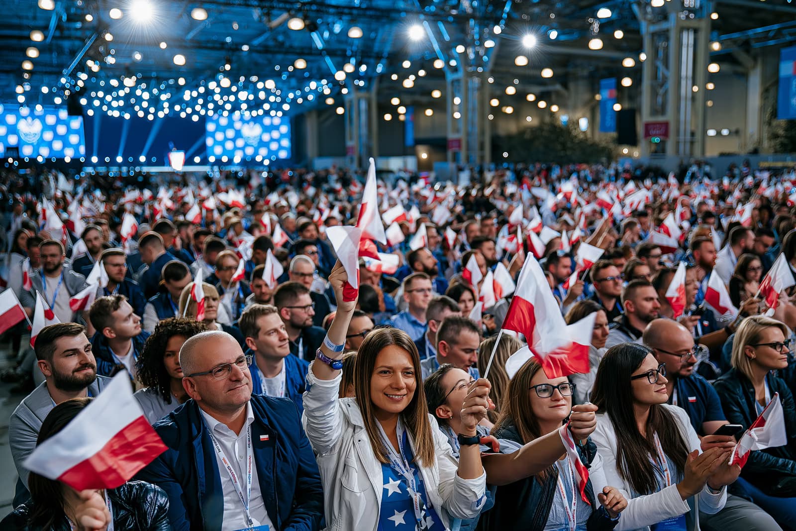 Uma multidão lotou o pavilhão de exposições, agitando pequenas bandeiras sob a forte iluminação do evento, no lançamento da campanha do AfD em Magdeburg, com um palco ao fundo.