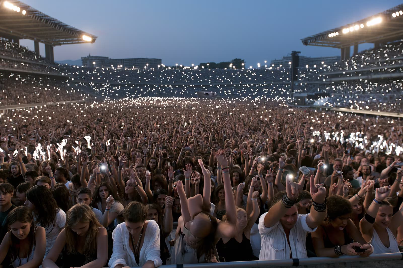 Uma grande multidão em um estádio iluminado pela luz do entardecer durante um concerto de verão em Munique.
