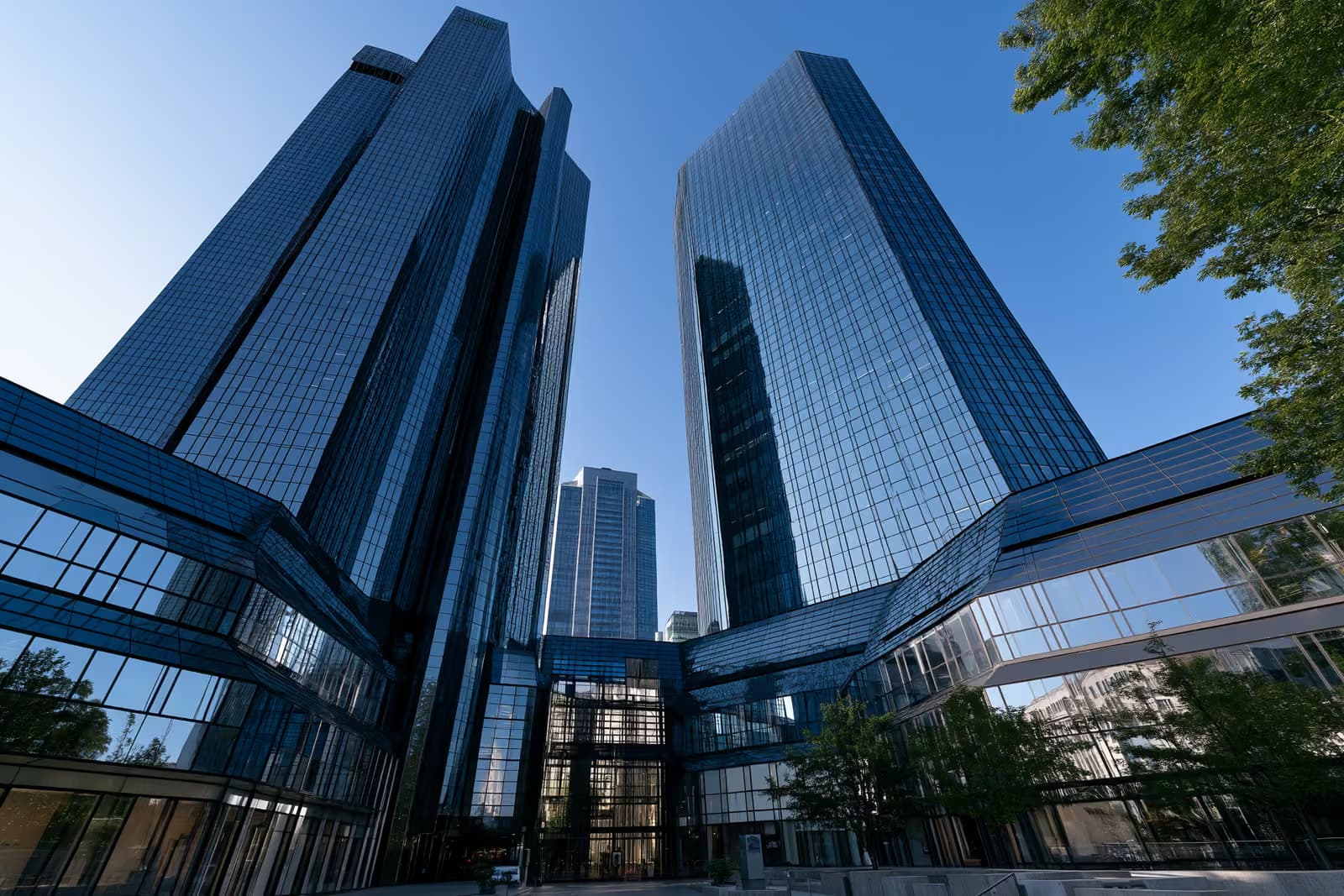 As duas torres gêmeas de vidro que compõem um banco em Frankfurt brilham contra um céu azul intenso, vistas de baixo.